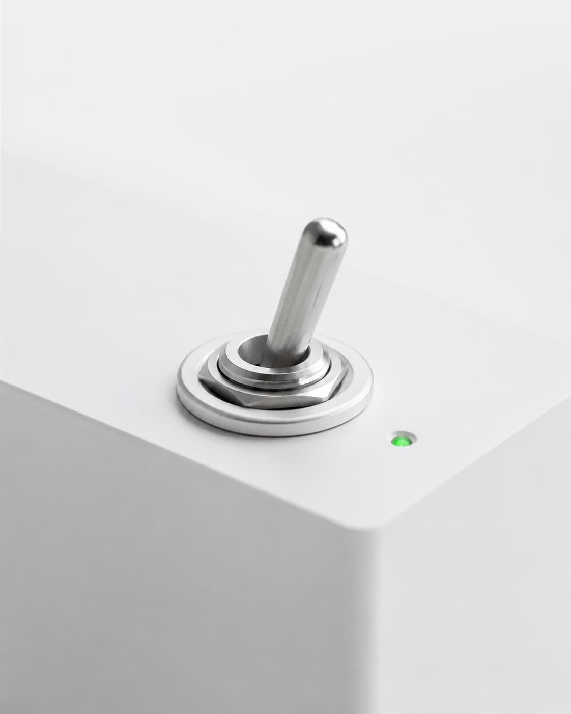 Machined aluminium toggle switch on a white panel, switched on beside a small green indicator light